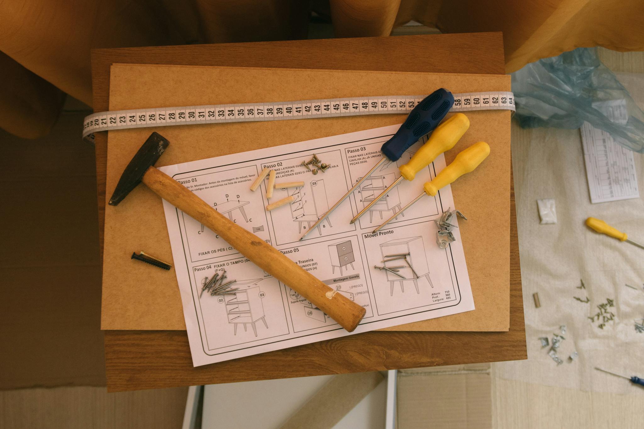 From above of paper instruction helping to assemble furniture with screwdrivers and hammer on top